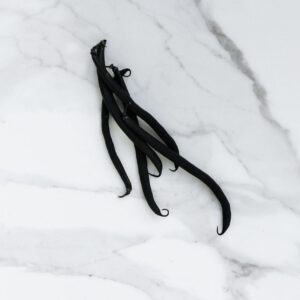 High-angle view of vanilla beans displayed on a white marble surface, exuding elegance.
